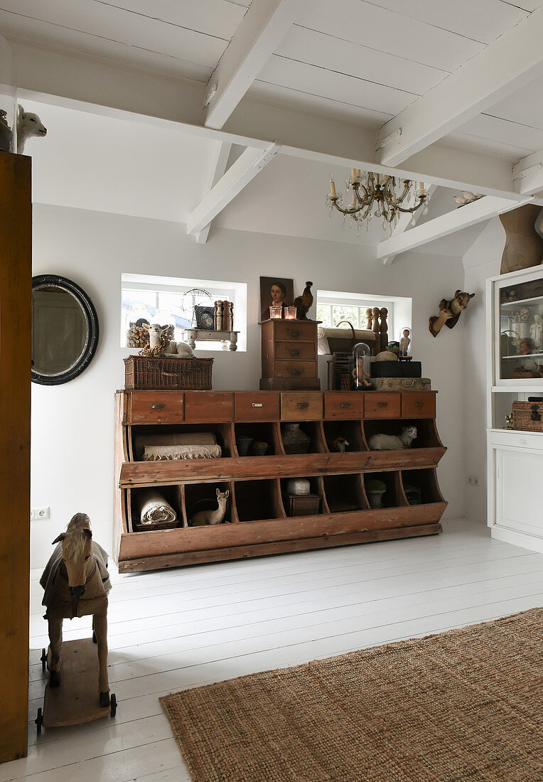 Antiker Holzschrank mit Schubladen und Regalfächern im Zimmer mit weißen Dielenboden