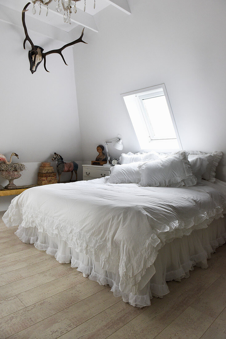 Doppelbett mit weißer Rüschendecke im Schlafzimmer mit Hirschgeweih an der Wand