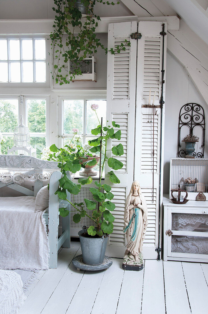 Mariastatue und Topfpflanze vor Schrank mit Lamellentür in weißem Wohnzimmer in Shabby-Style