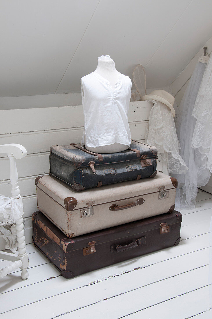 A stack of vintage suitcases and a dressmaker's dummy in an attic