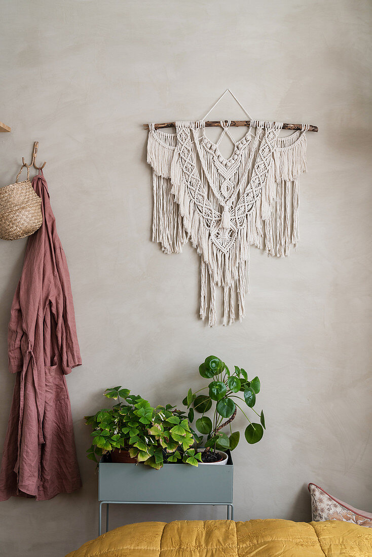 Plant stand below macramé handing on lime-washed wall