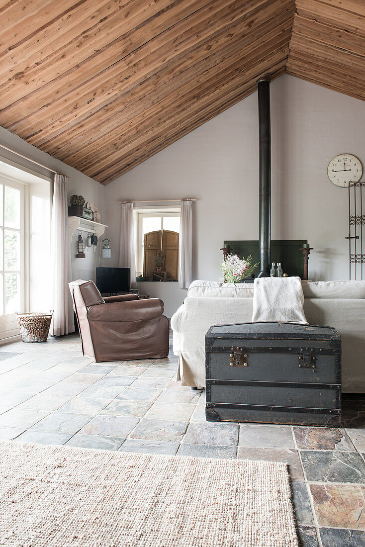A wooden chest behind a sofa and an armchair in an open-plan living room in a former farmhouse