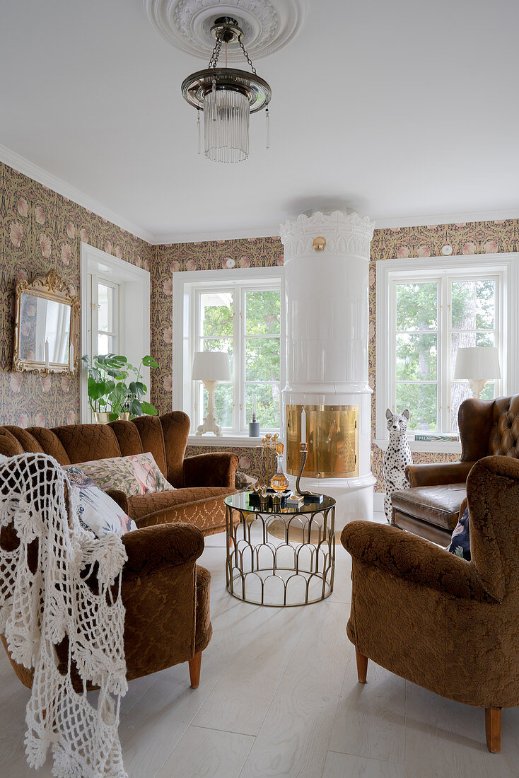 Antique upholstered suite and Swedish tiled stove in the living room with floral wallpaper