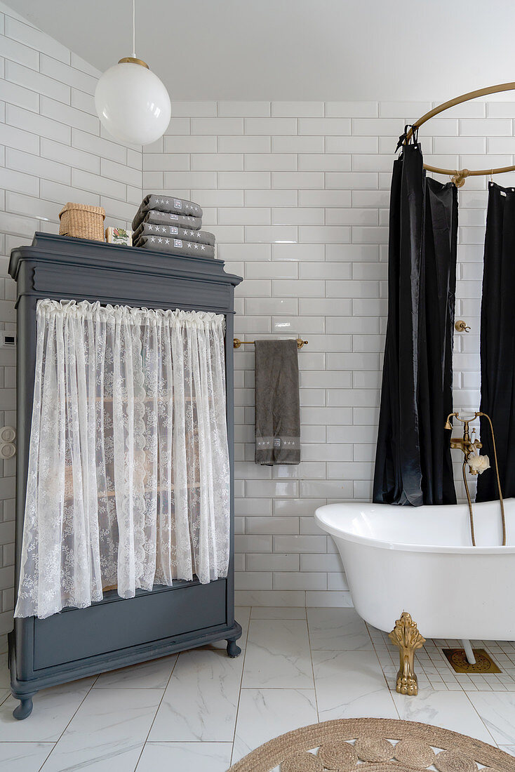 A cupboard with a curtain and a freestanding bathtub in a bathroom with white subway tiles