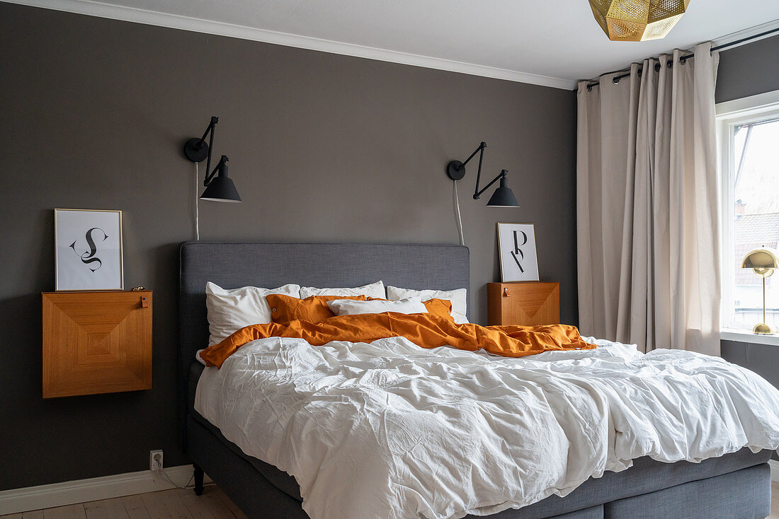 A double bed, bedside tables and wall lights in a bedroom with a dark wall