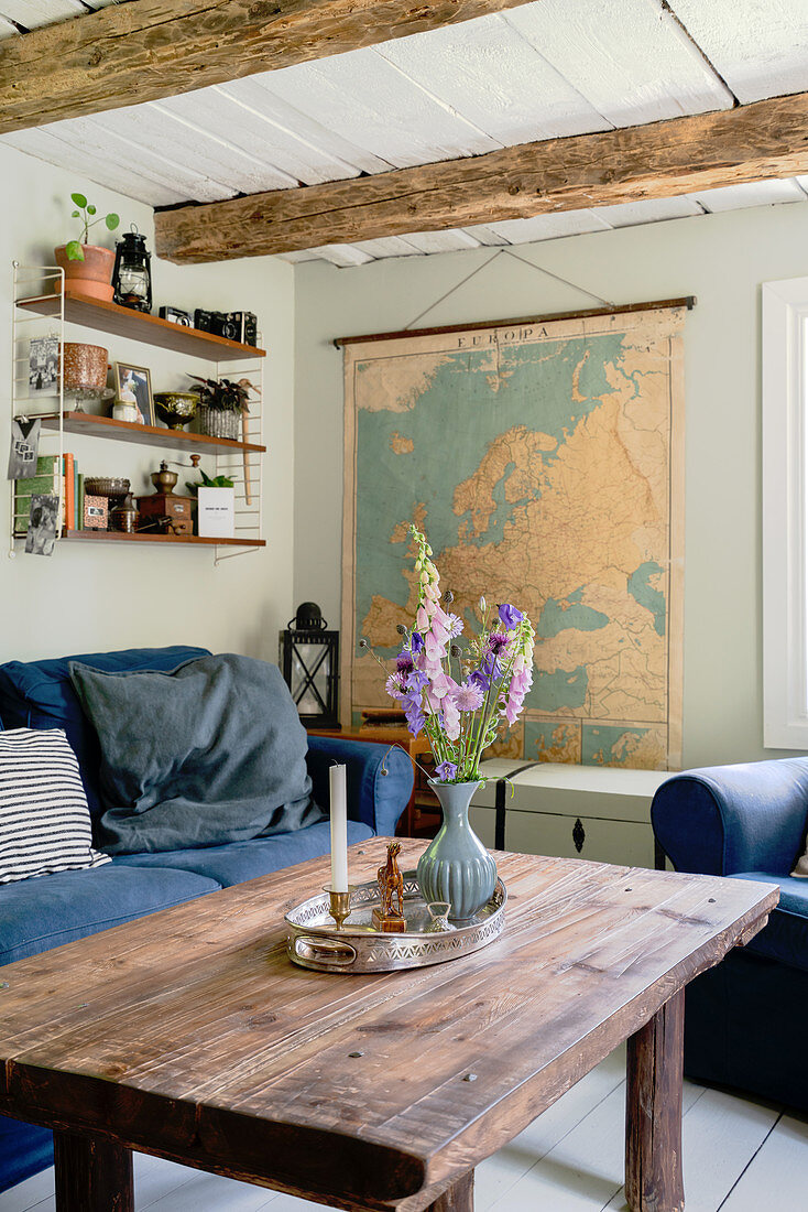 Rustikaler Couchtisch, Sofa mit blauer Husse und Europatkarte in ländlichem Wohnzimmer