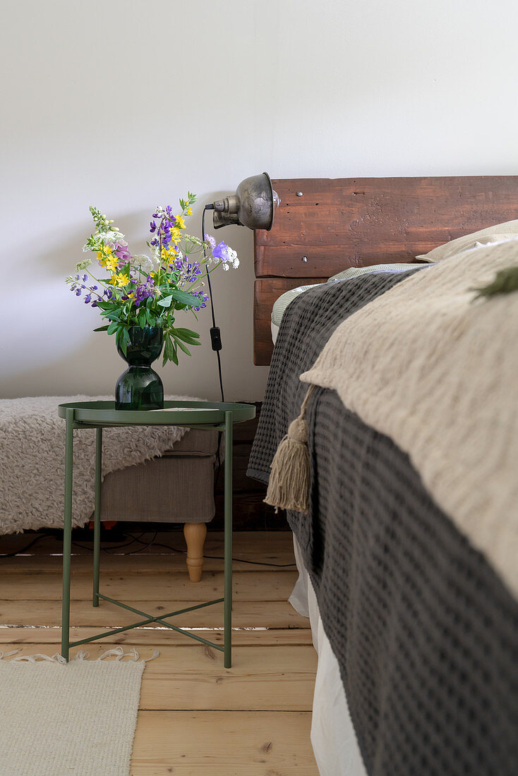 Blumenstrauß auf Nachttisch neben Bett mit Kopfteil aus recycltem Holz