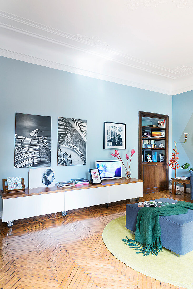 Black-and-white photos on a blue wall above a lowboard in old-style living room with a parquet floor
