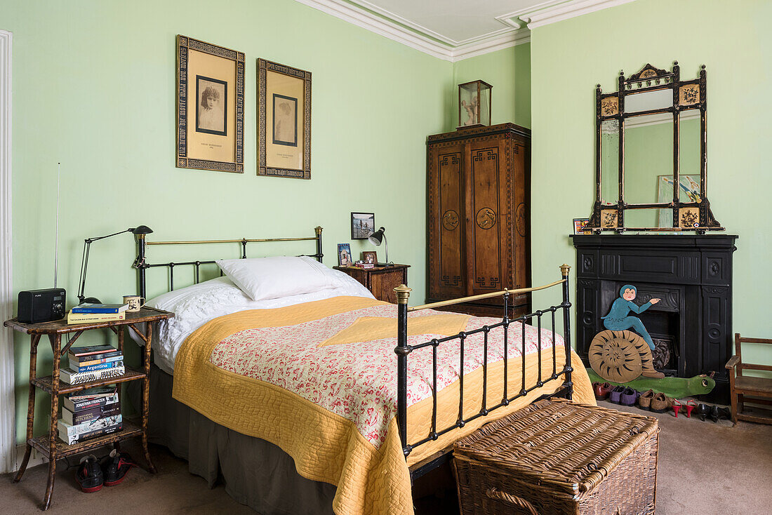 Original prints hang above French iron bed with Arts and Crafts ebonised and gilt mirror
