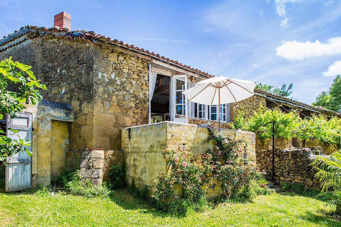 Stone house with sunny garden and parasol on terrace