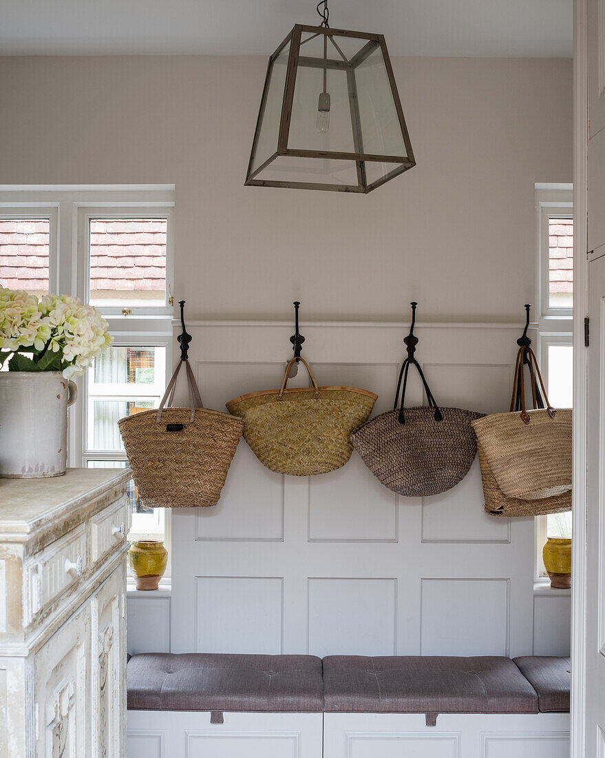 A selection of French wicker shopping baskets on iron coat hooks in boot room with pendant lamp