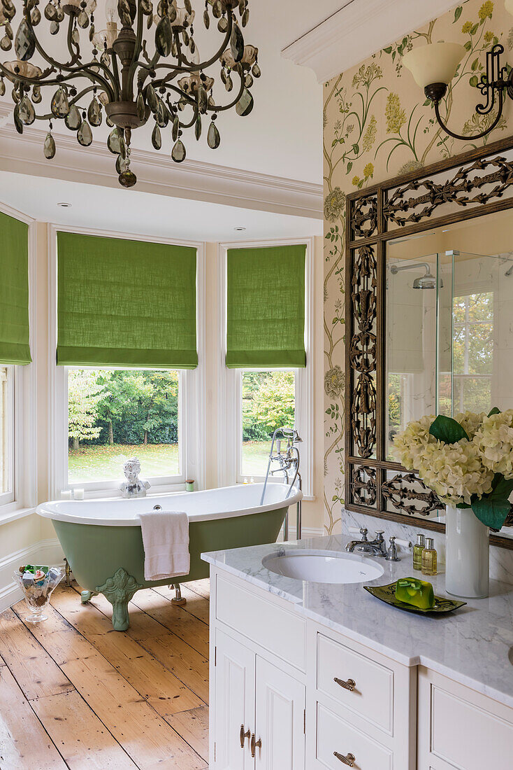 Freistehende Badewanne am Erkerfenster mit grünen Jalousien, im Vordergrund Waschtisch