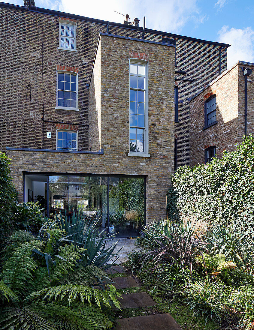 Ferns and yuccas in lush garden of brick house with extension