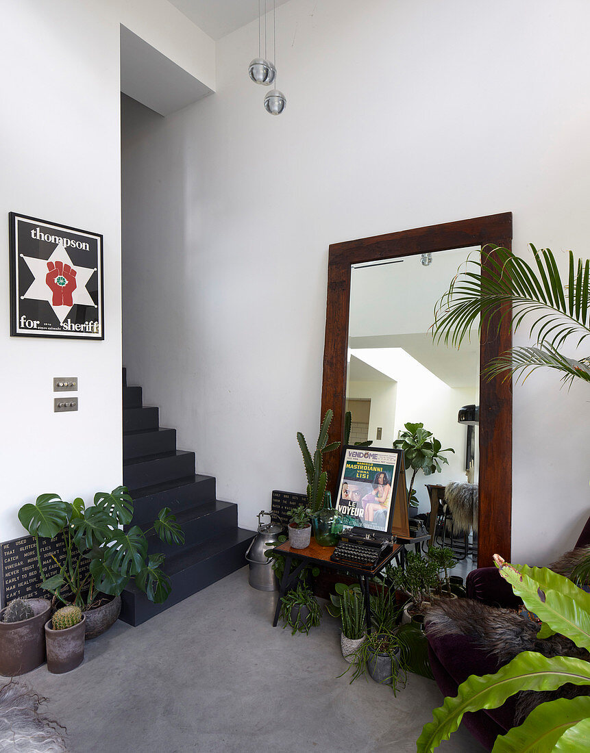 Floor-standing mirror and collection of houseplants at foot of grey staircase