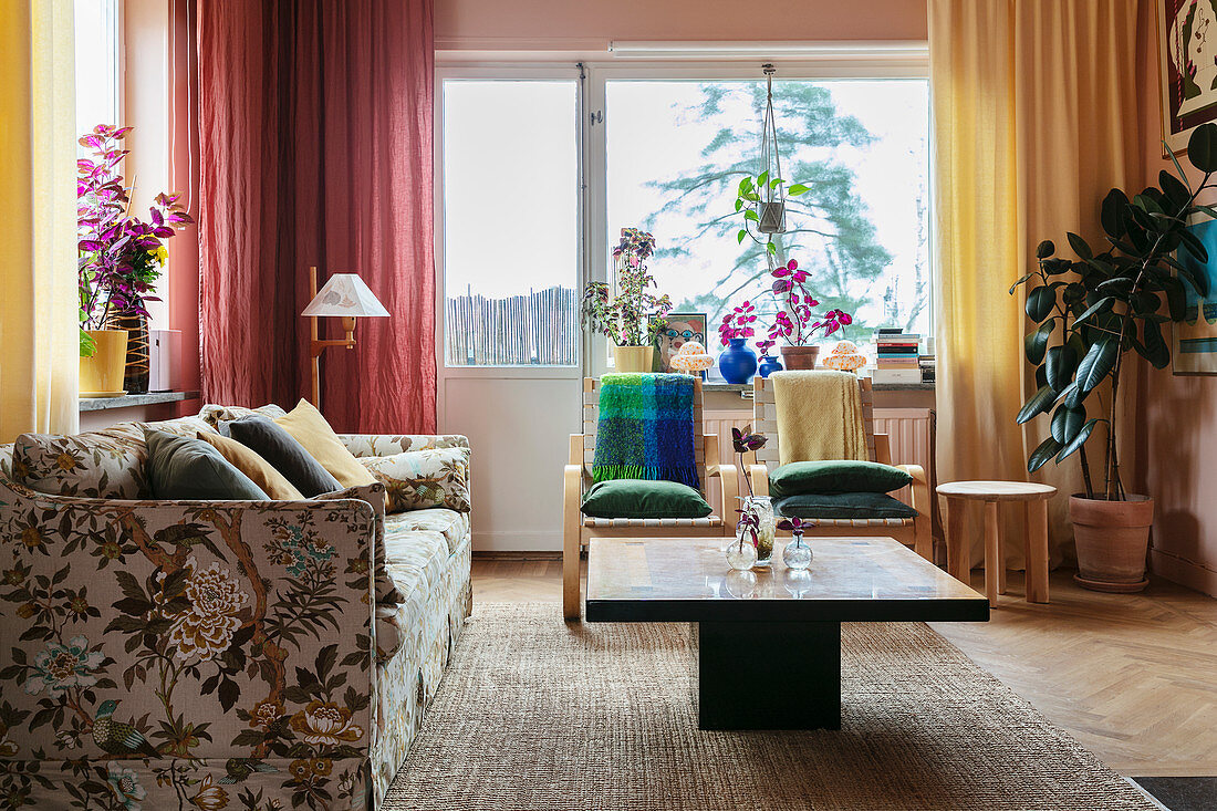 An upholstered sofa with a floral pattern, a coffee table and colourful curtains in a living room