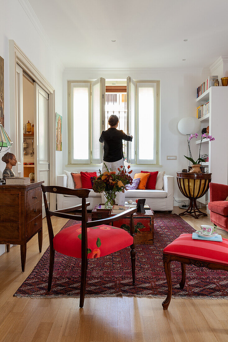 Rote Stühle, antike Kommode, Truhen als Couchtisch und Sofa im Wohnzimmer, Frau im Hintergrund