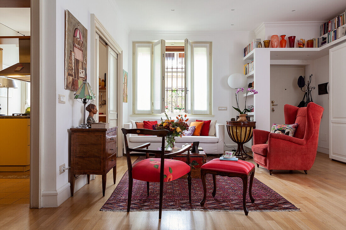 Red chairs, antique chest of drawers, chests used as coffee table, sofa and armchair in living room