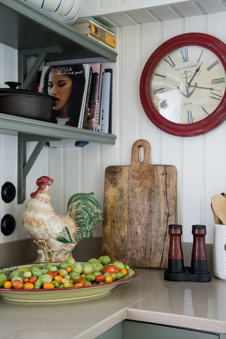 Küchenarbeitsplatte übereck mit Holzbrett, Hahnfigur und Gemüseteller, darüber Wanduhr