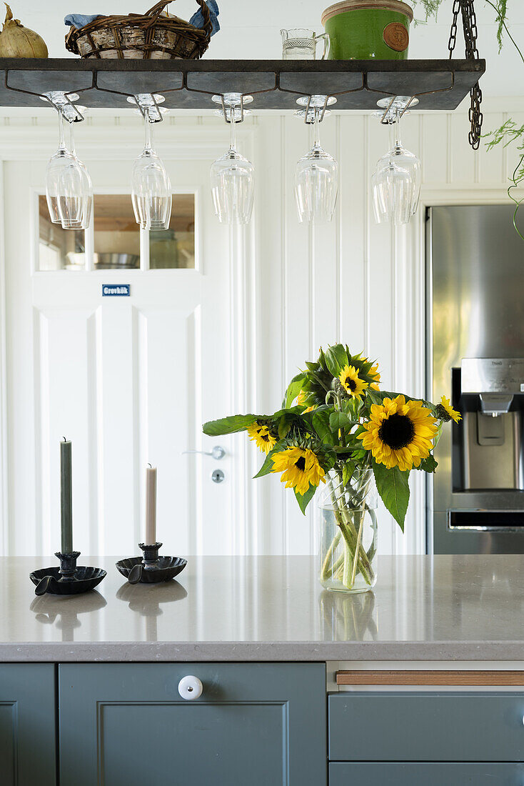 Iron shelf with wine glasses above kitchen unit with bouquet of sunflowers
