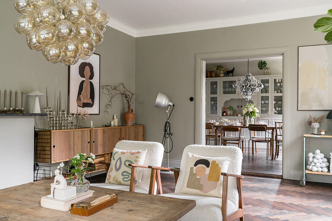 Couchtisch aus Holz mit weiß bezogenen Sesseln, im Hintergrund Sideboard und Blick in das Esszimmer