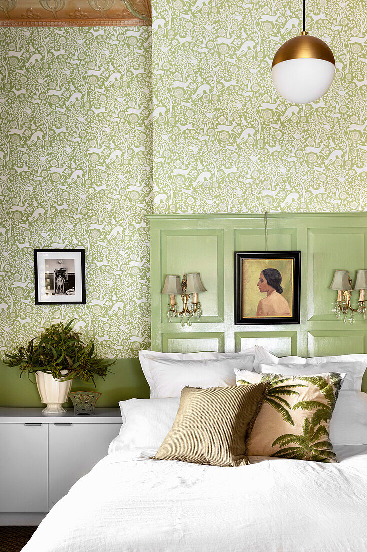 Doppelbett mit Kissen vor grüner Holzvertäfelung und grün gemusterter Tapete im Schlafzimmer
