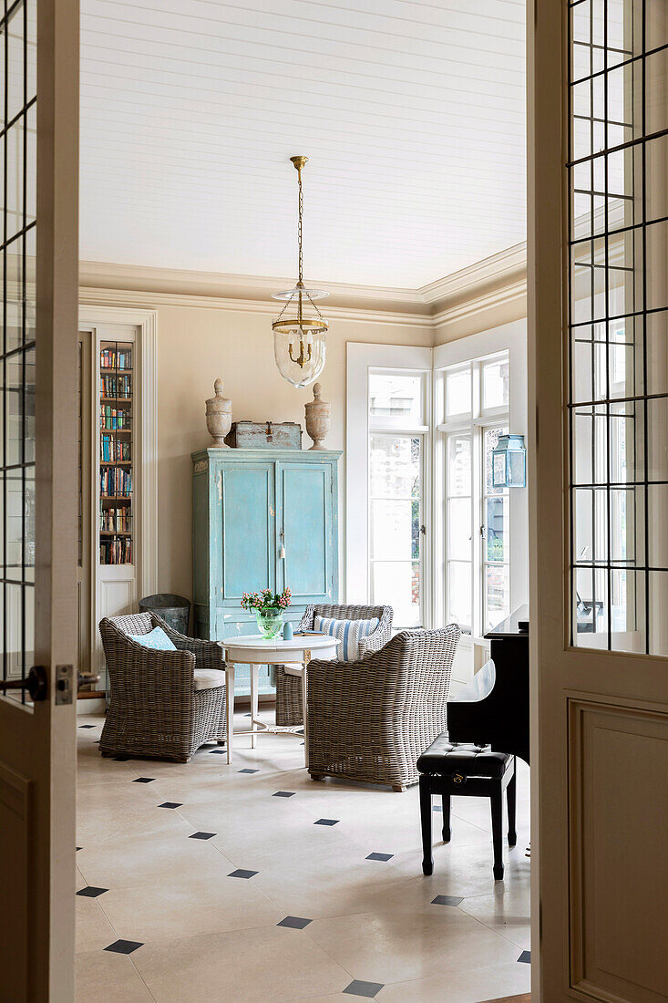 View into the drawing room with round table, rattan armchairs, and blue cupboard, limestone floor tiles
