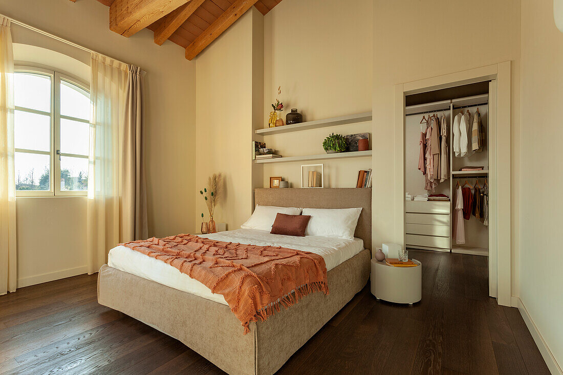 Schlafzimmer mit Doppelbett, darüber Regale und begehbarer Kleidreschrank