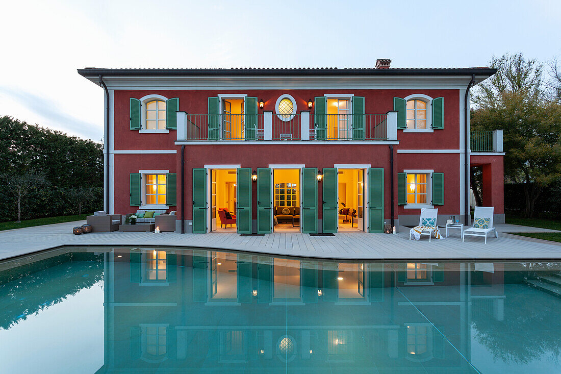 A view across a pool of a two-storey villa with green shutters