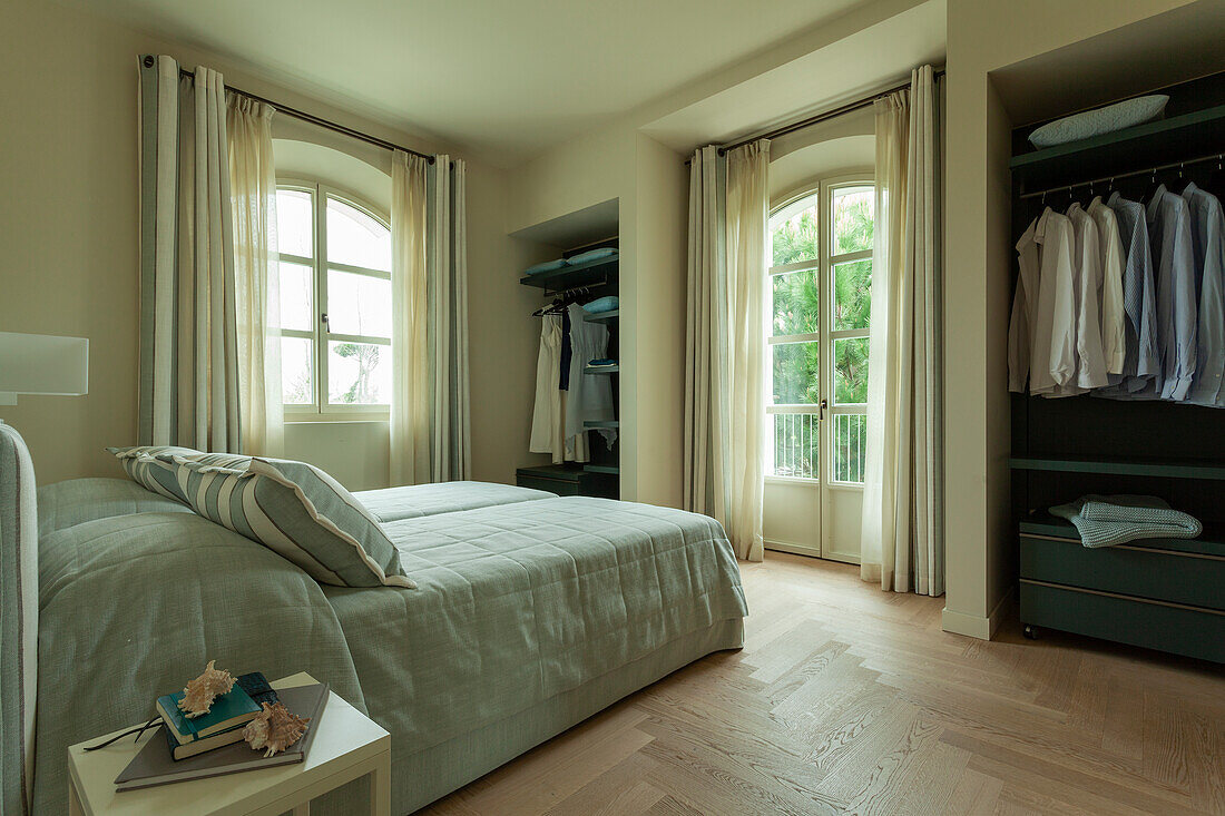 Bett mit mintgrüner Tagesdecke und offene Kleiderschränke im Schlafzimmer