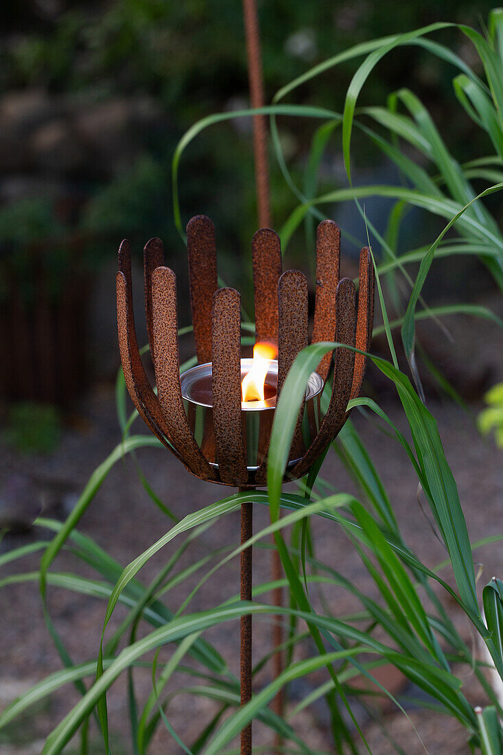 Rostiger Kerzenhalter mit brennender Kerze im Garten