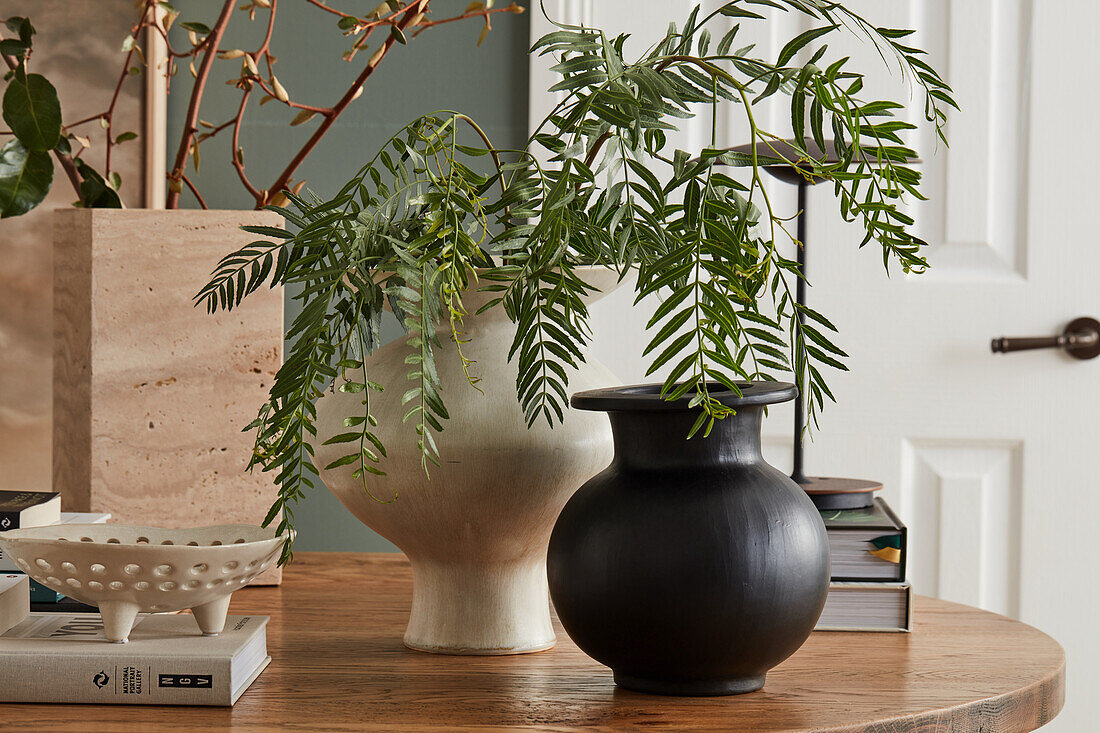 Verschiedene Vasen mit Blätterzweigen auf rundem Tisch