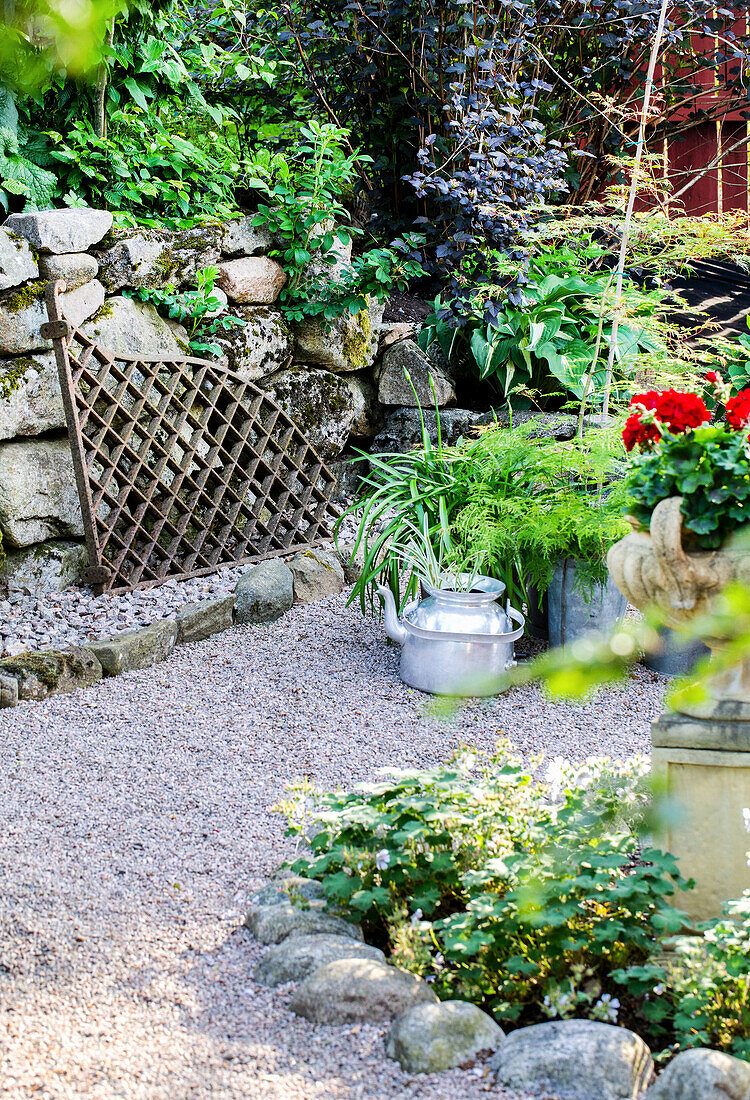 Decoratively designed gravel area with trellis fence, decorative tea kettle and plants
