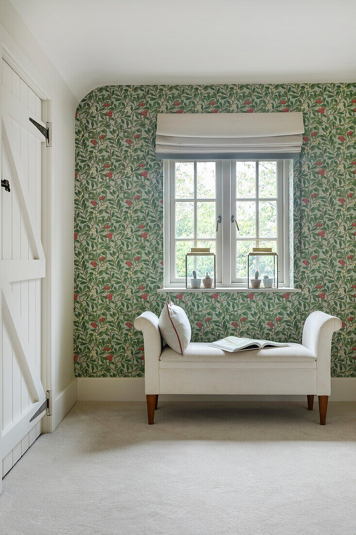 Chaise lounge under window in front of wallpapered wall