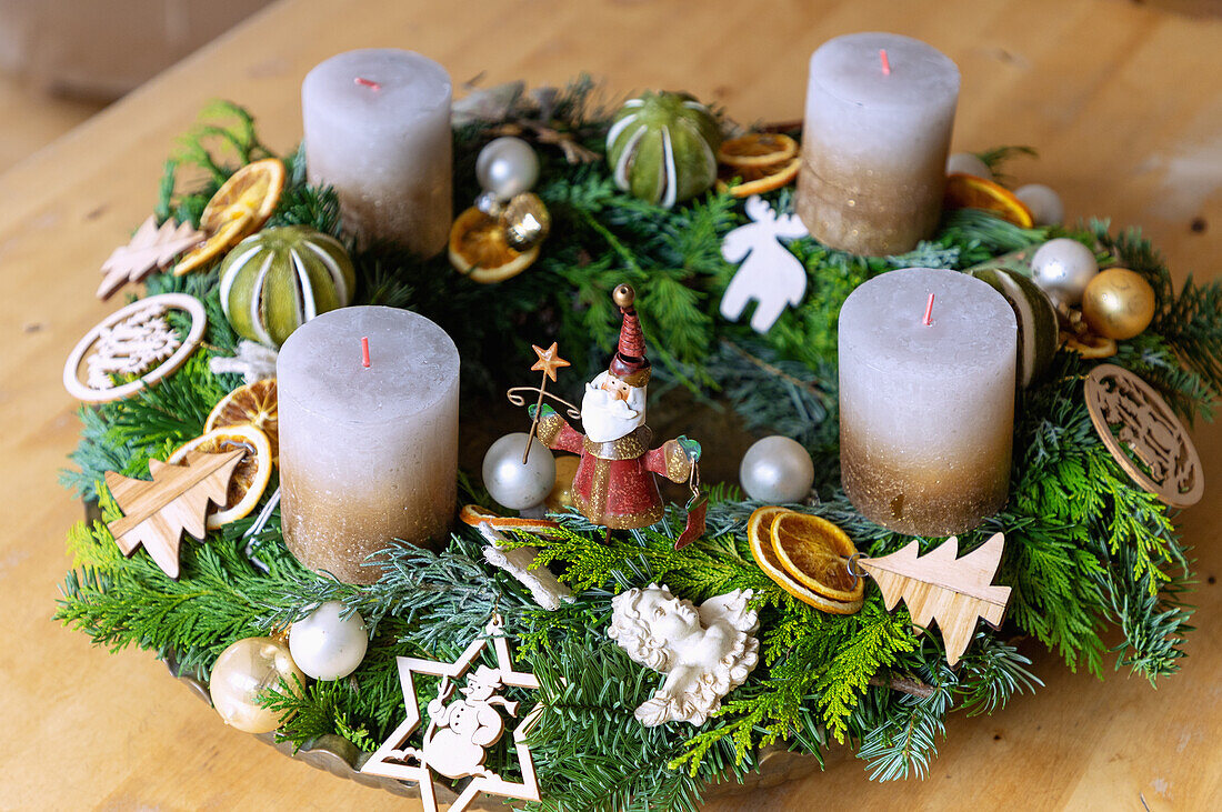 Mit Naturschmuck, Holzschmuck und Blechfiguren dekorierter Adventskranz aus gemischten Tannen- und Koniferenzweigen und goldweißen Kerzen
