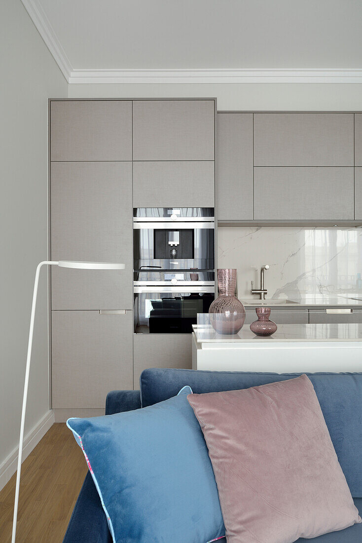 Offener Wohnraum mit blauem Sofa, im Hintergrund eingebaute Küche