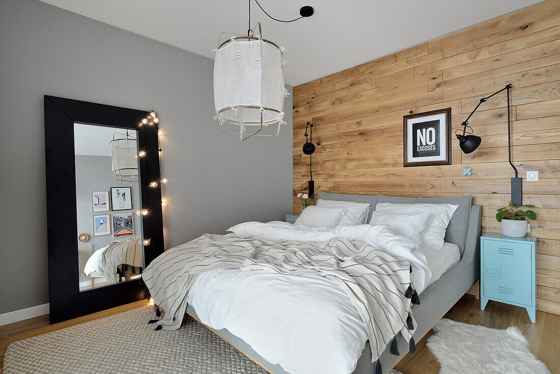 Double bed in front of plank wall in bedroom, large mirror with fairy lights in front of grey wall