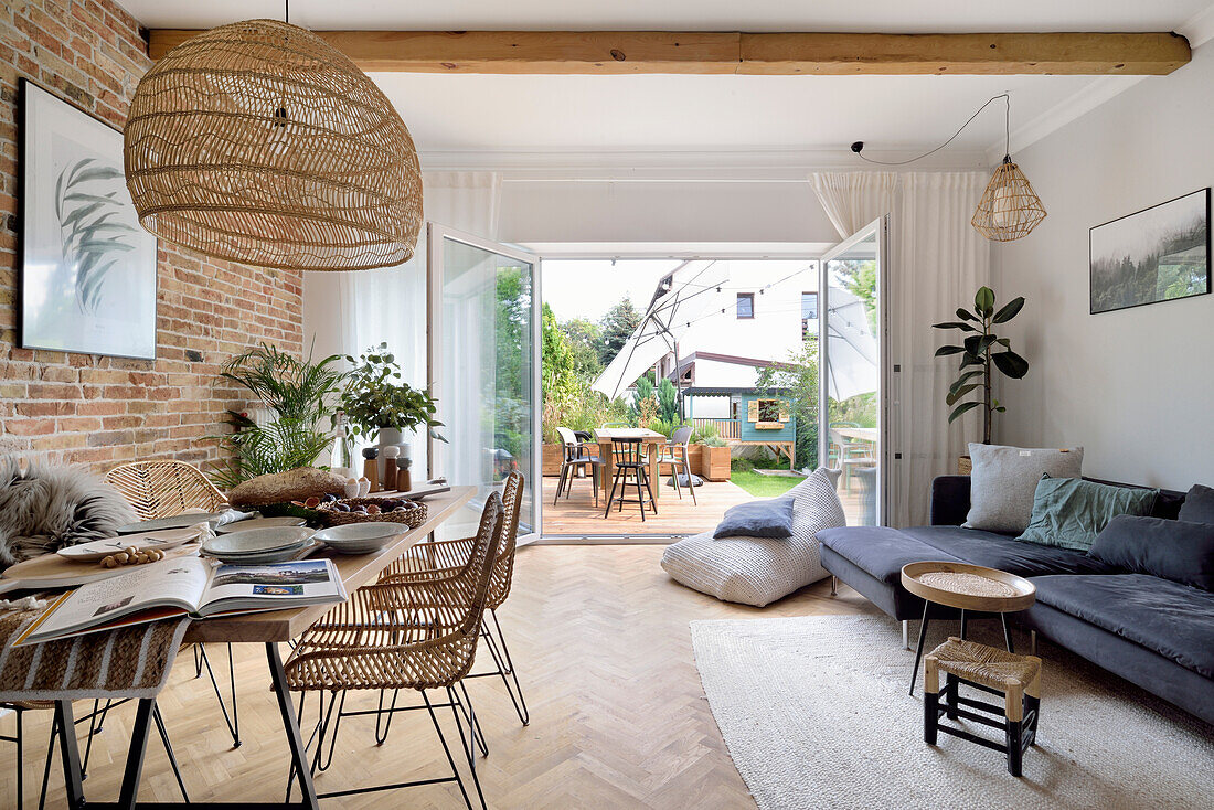 Open living room with brick wall and terrace access, dining table in the foreground, woven pendant light above it