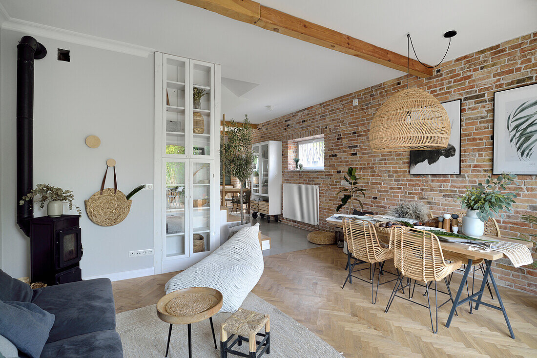 Open living room with dining table in front of brick wall, woven pendant light above it