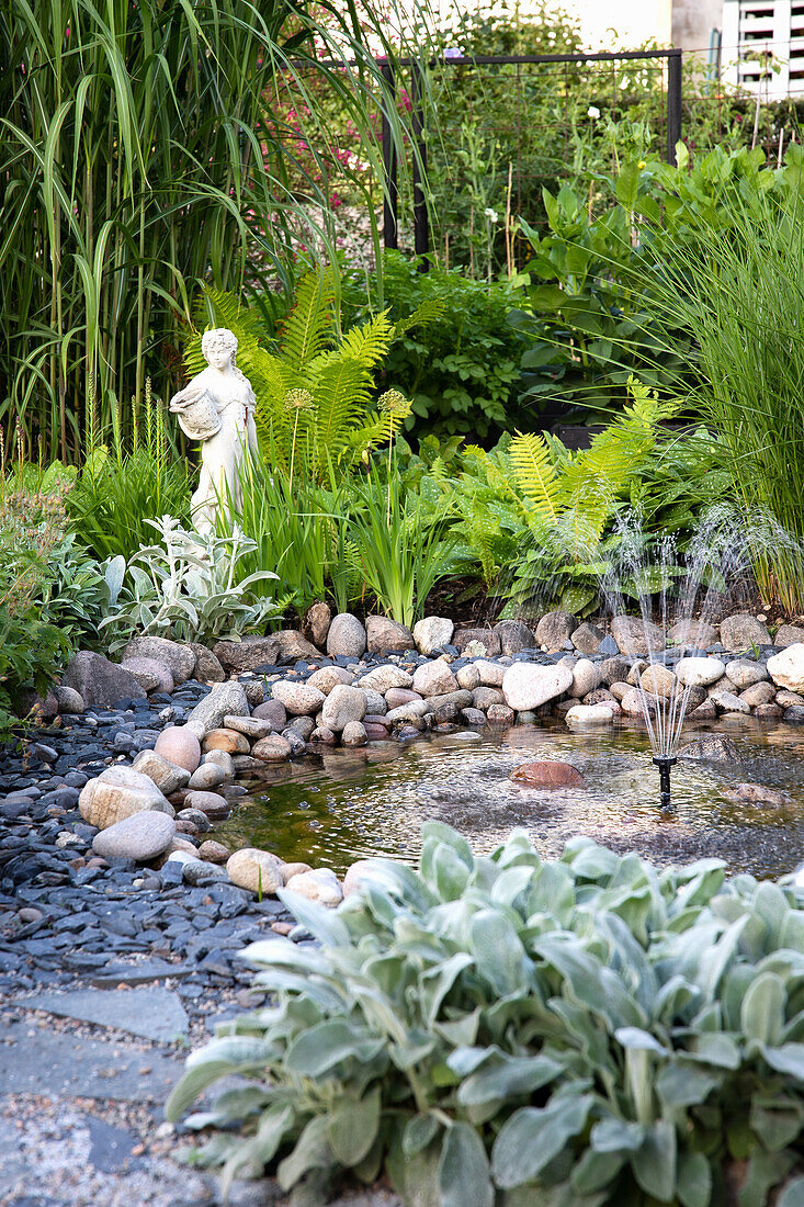 Kleiner Teich mit Kieselsteinen und Statue im Garten