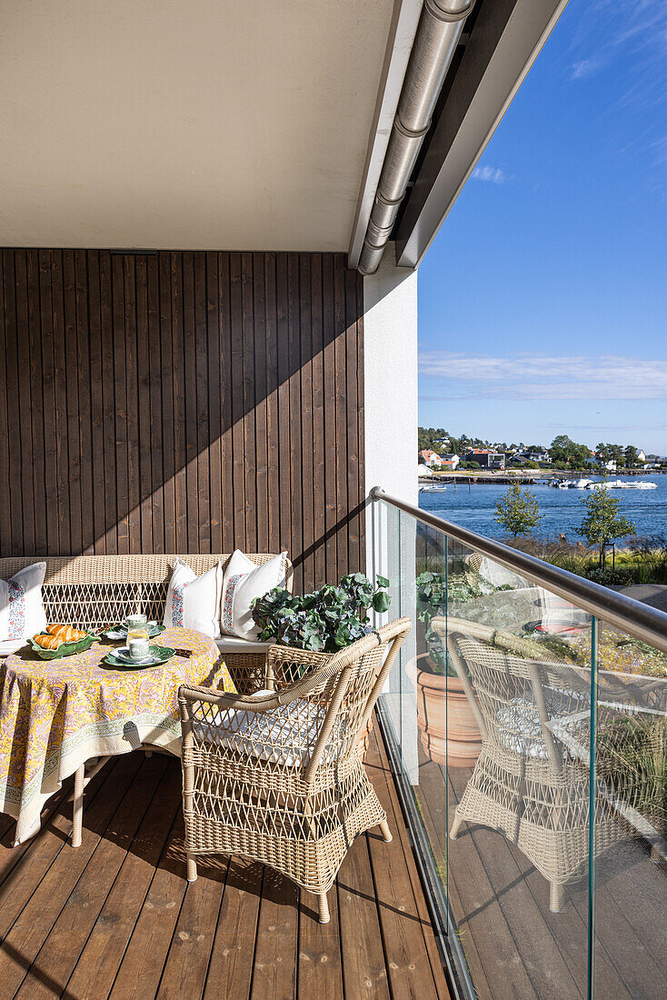 Rattanmöbel und Tisch auf überdachter Terrasse mit Glasbalustrade