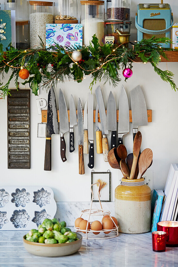 A magnetic knife rack under a kitchen shelf decorated for Christmas