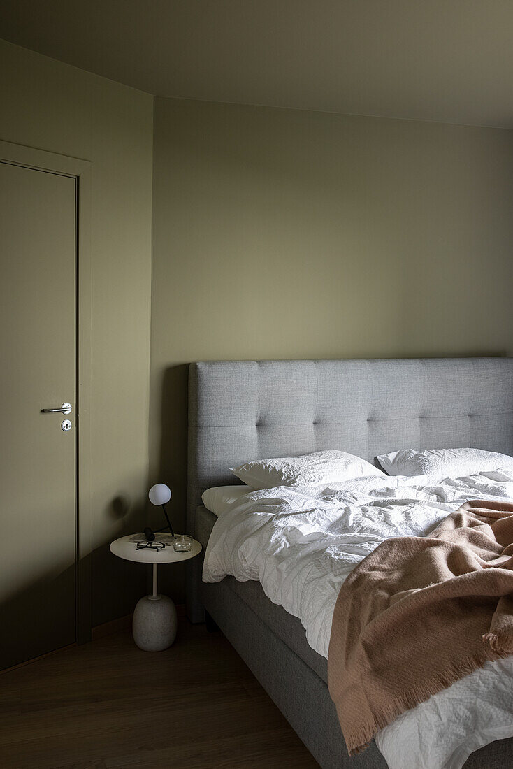 Doppelbett mit grauer Polsterung im grünen Schlafzimmer