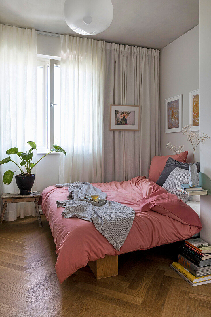 Doppelbett im Schlafzimmer mit bodenlangen Vorhängen und Kunstwerken