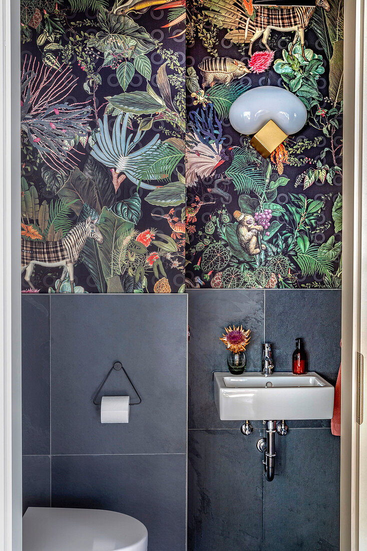 Guest bath with grey wall tiles and wallpaper with jungle motif