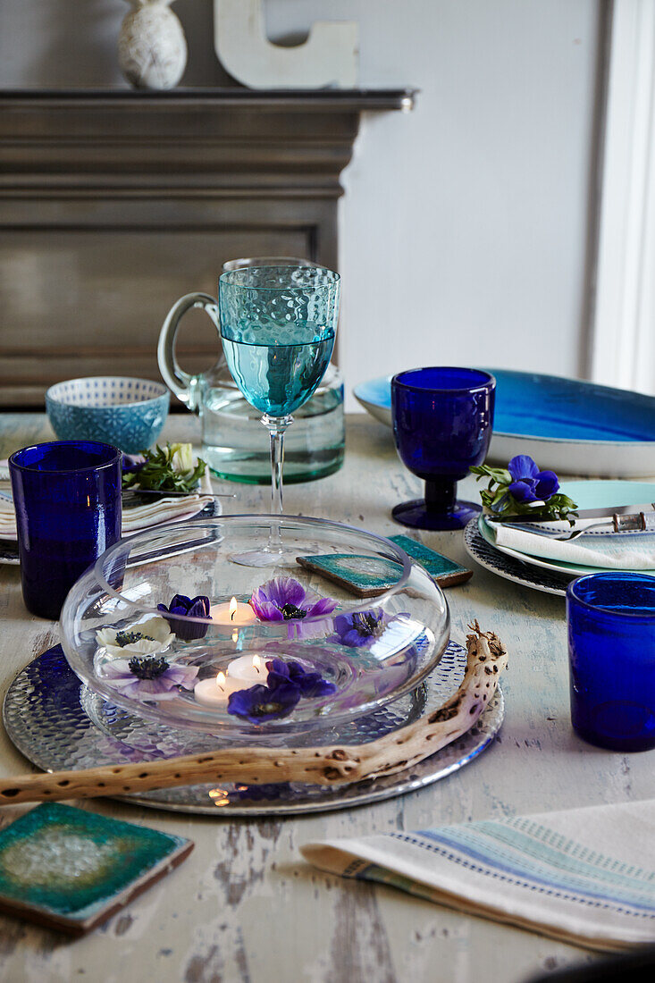 Gedeckter Tisch in Blautönen, Glasschale mit Schwimmkerzen und Blüten
