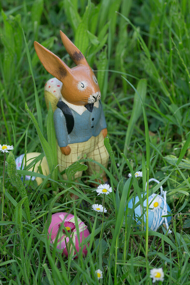 Easter bunny made of wood, in the green grass, Easter eggs with daisies and daisies