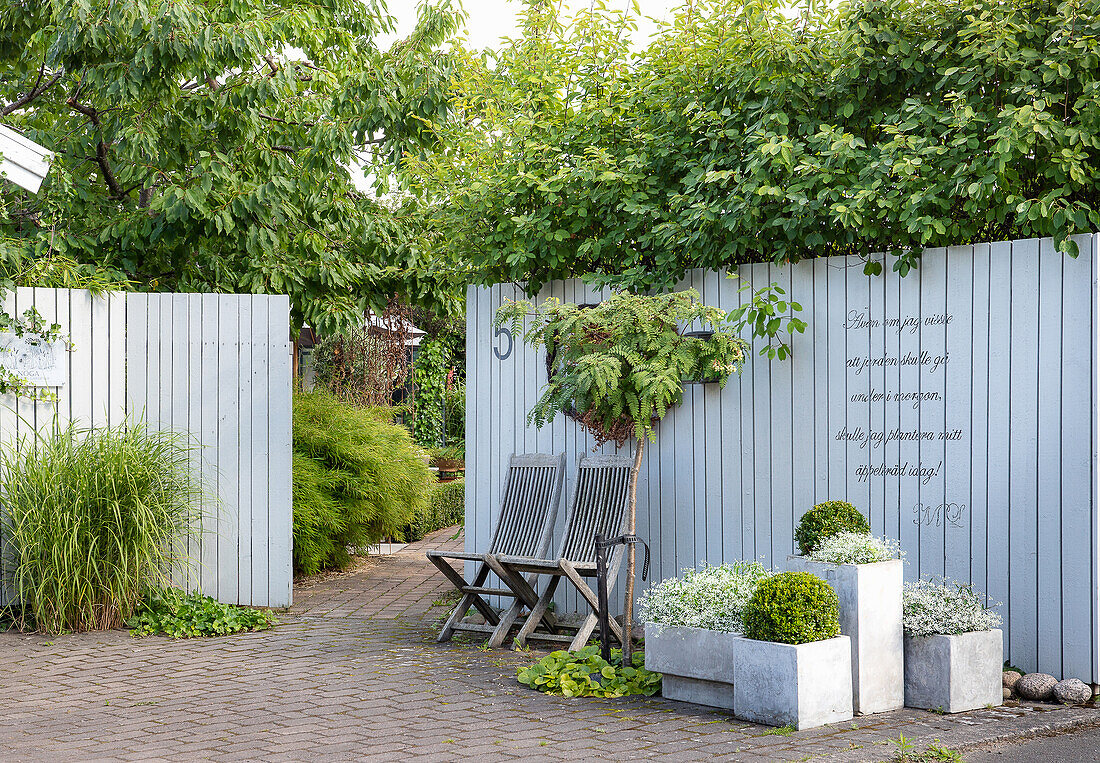 Plant pots and wooden chairs in front of wooden fence with writing