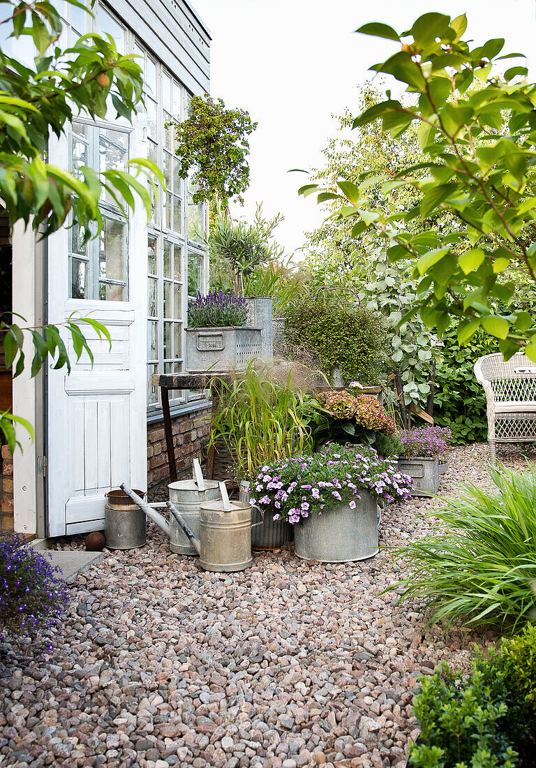 Watering cans and plant pots on gravel in front of the greenhouse