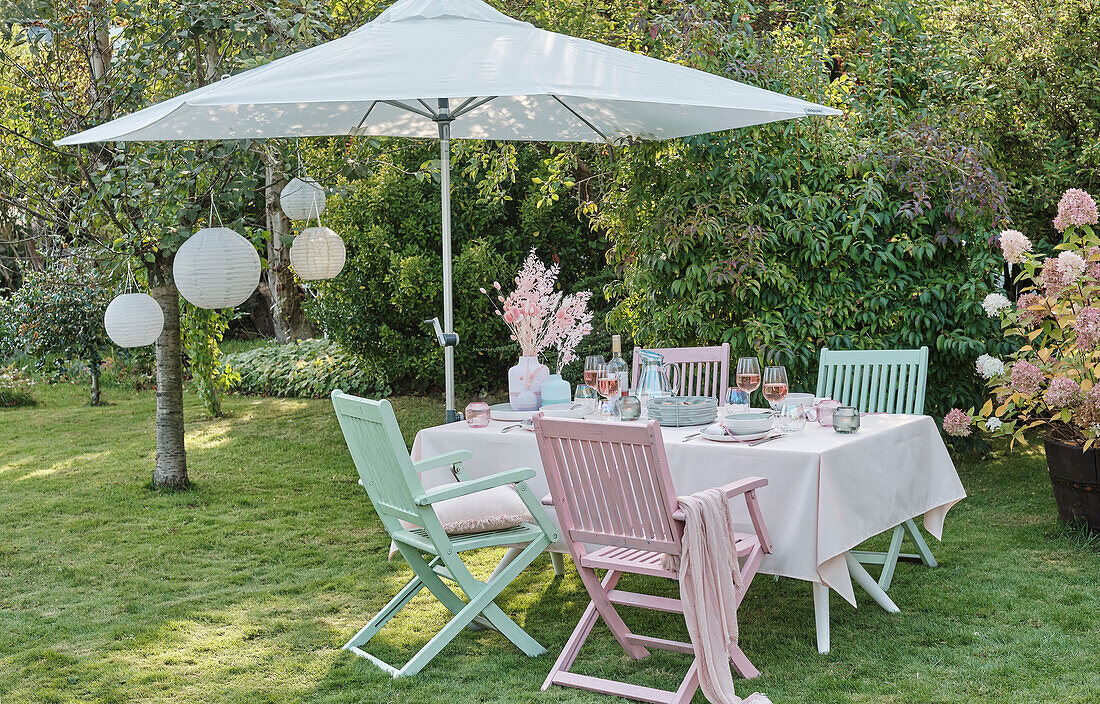 Gedekter Tisch in Pastelltönen, Sonnenschirm und Lampions im Garten