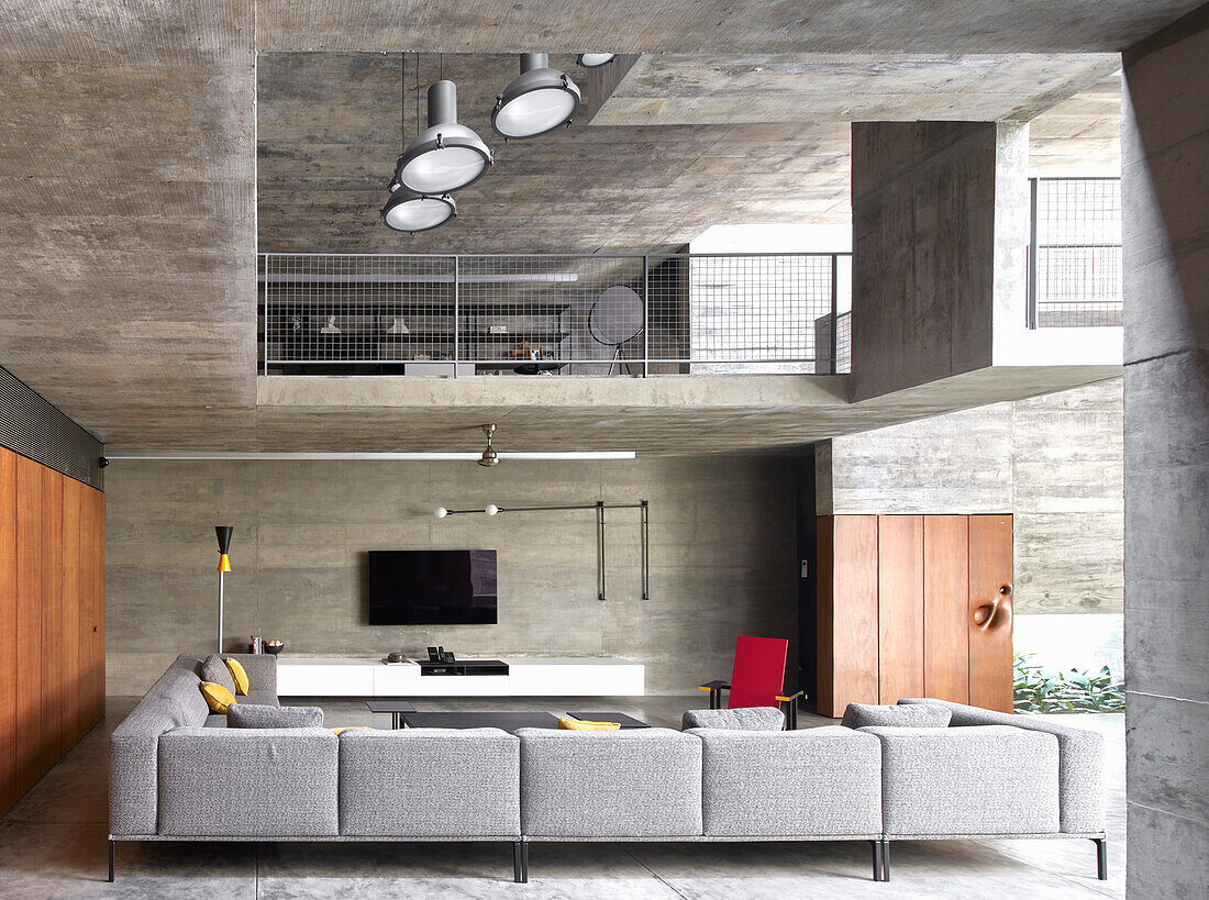 Ground floor with sitting area, built-ins and view of mezzanine in a concrete house